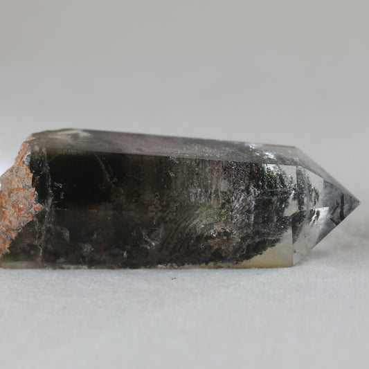 A polished freeform crystal of garden quartz with a clear center and a brownish-gray rim.