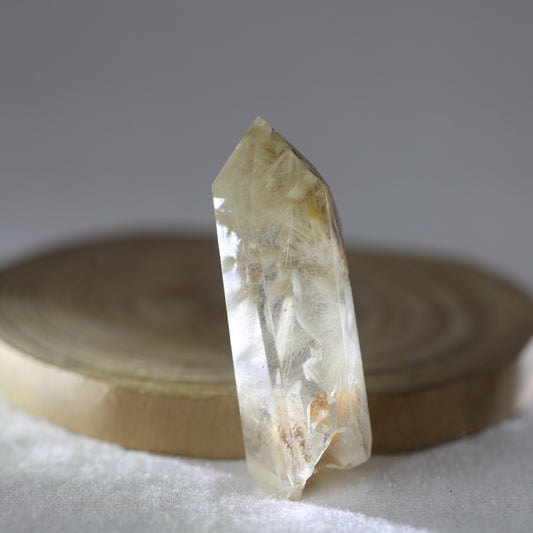 A free-form Golden Rutile Quartz gemstone with visible golden rutile inclusions, placed on a wooden surface.