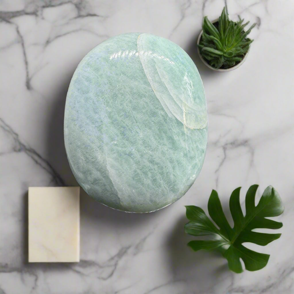 An Amazonite Palm Stone placed on a marble surface, surrounded by a small potted plant and a paper coaster.
