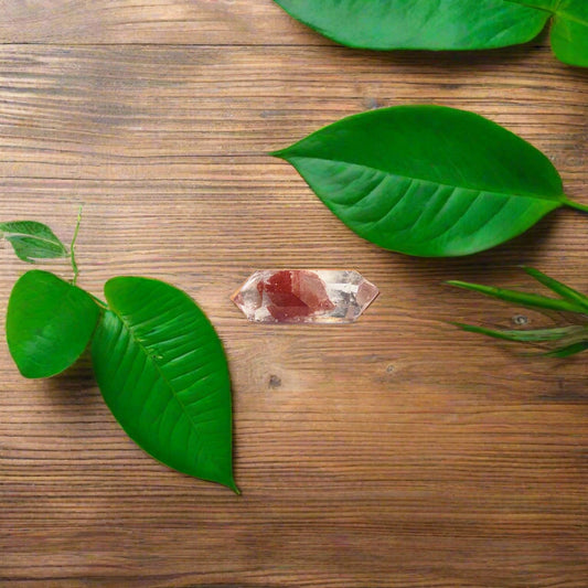 A freeform red phantom quartz crystal on a brown paper, with a cup of coffee and a green leaf in the background.