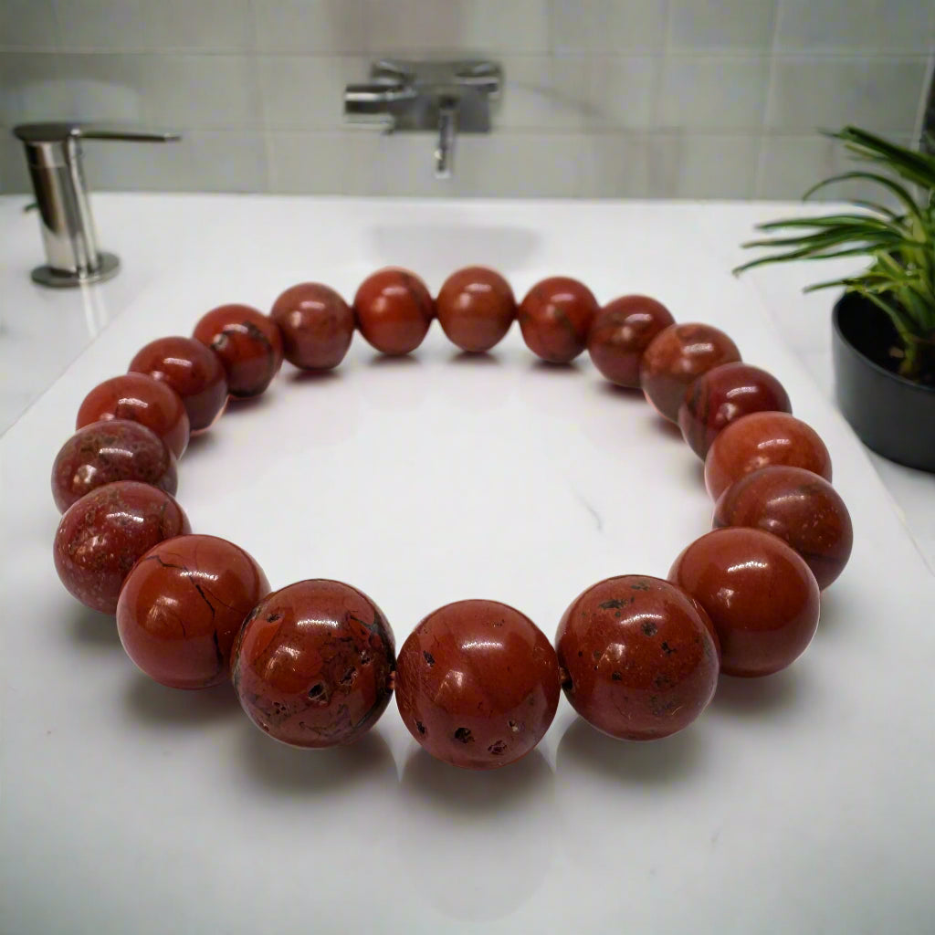 A red jasper bracelet laid out on a flat surface, displaying its beaded structure and solid red color.