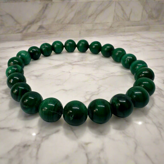 A bracelet made of polished malachite beads laid out on a marble surface.