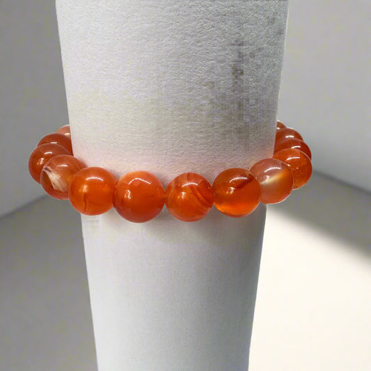 A bracelet made of round red carnelian beads displayed on a white stand.