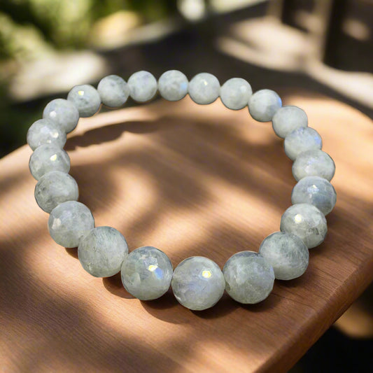 A bracelet made of round rainbow moonstone beads with a diamond cut, displayed on a wooden surface.