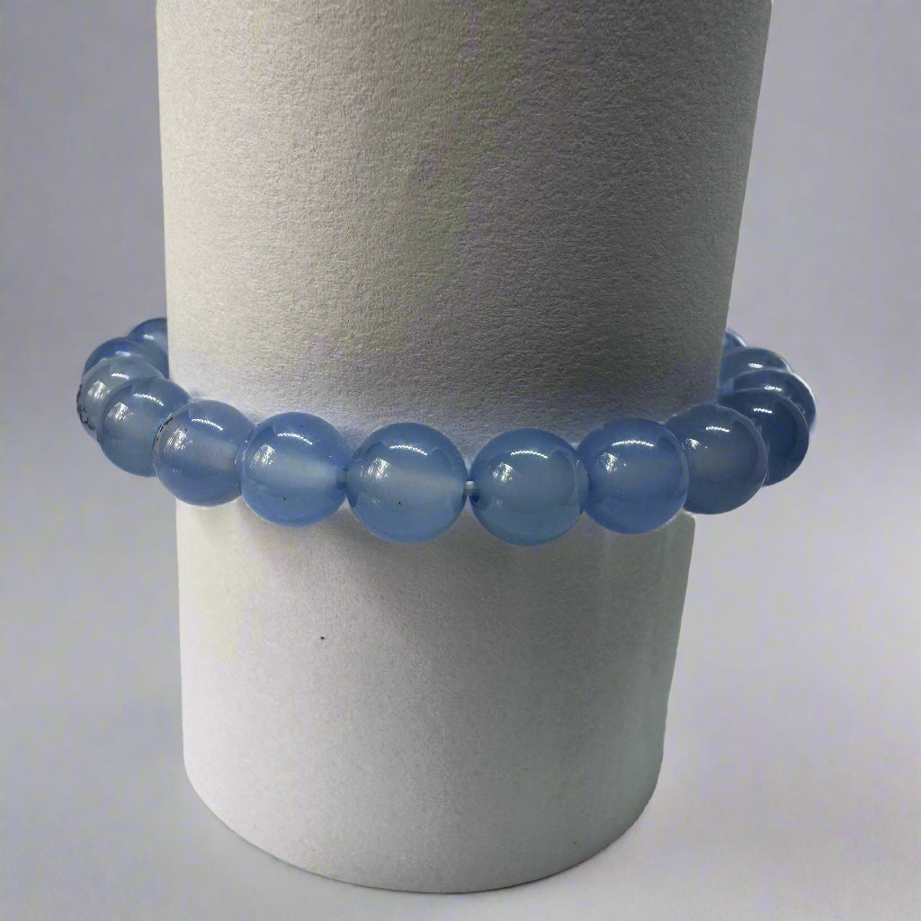 A blue chalcedony bracelet with 8mm round beads displayed on a cylindrical stand.