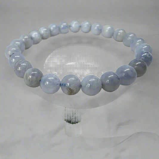 A blue lace agate bracelet with 8mm beads displayed on a clear stand.