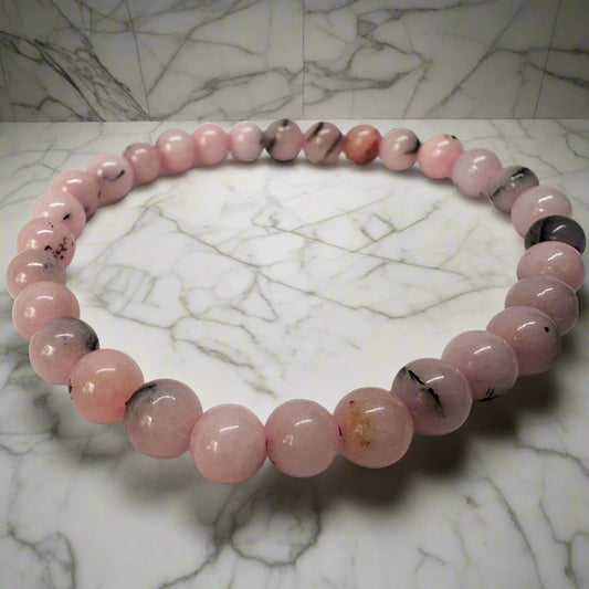A pink opal bracelet with 6mm beads displayed on a marble surface.