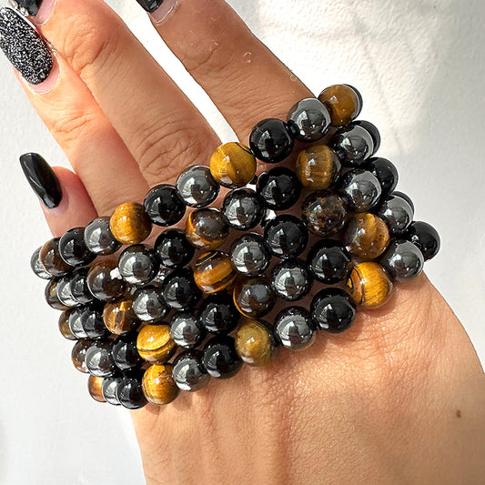 A person's hand wearing a multicolored beaded bracelet made of black and amber beads.