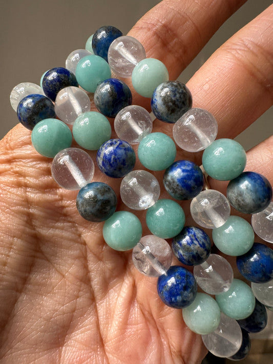 A hand holding a communication bracelet with multicolored beads, including shades of blue, green, and clear.