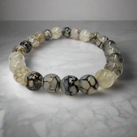 A bracelet made of round Dragon Vein Jasper stones, displayed on a marble surface.