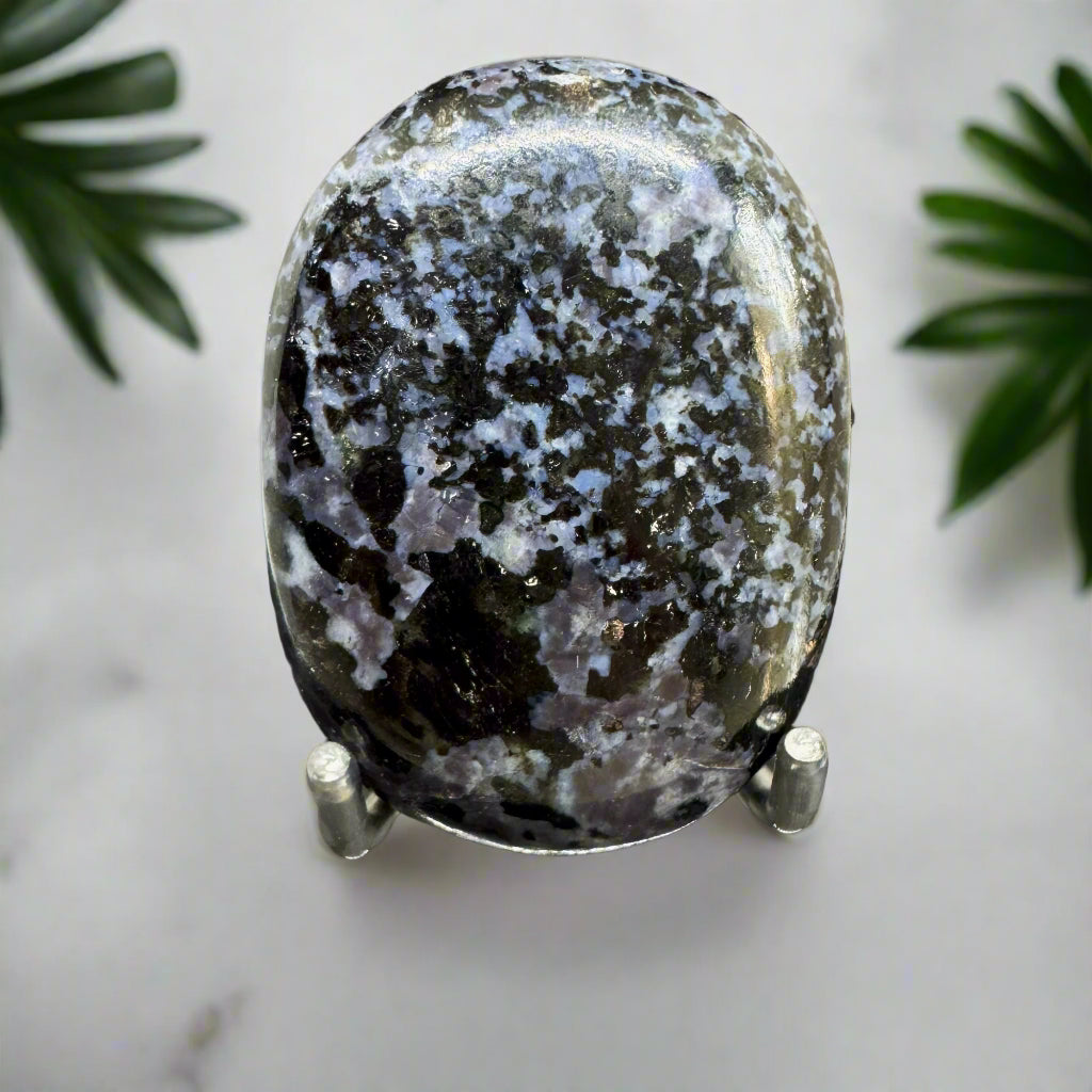 An oval-shaped Indigo Gabro palm stone on a stand, displaying deep indigo tones with lighter shades of gray and black patterns.