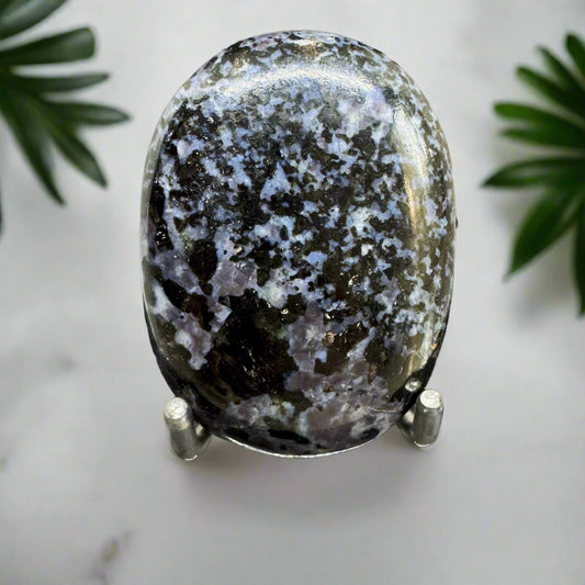An oval-shaped Indigo Gabro palm stone on a stand, displaying deep indigo tones with lighter shades of gray and black patterns.