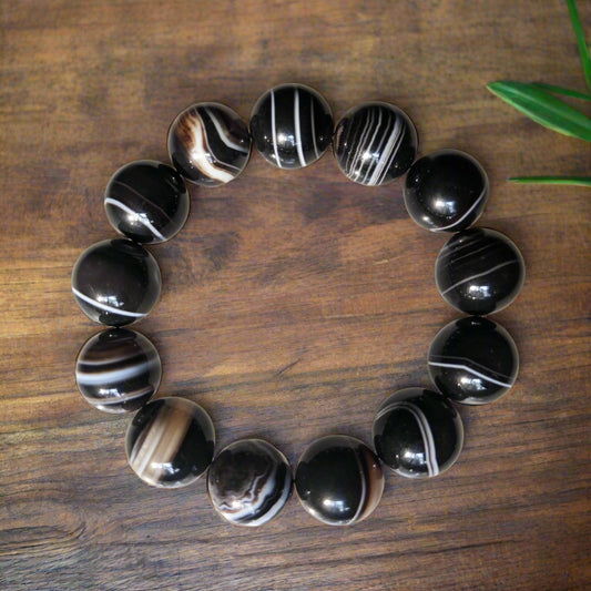 A Black Sulemani Bracelet with 15mm beads laid out on a wooden surface.