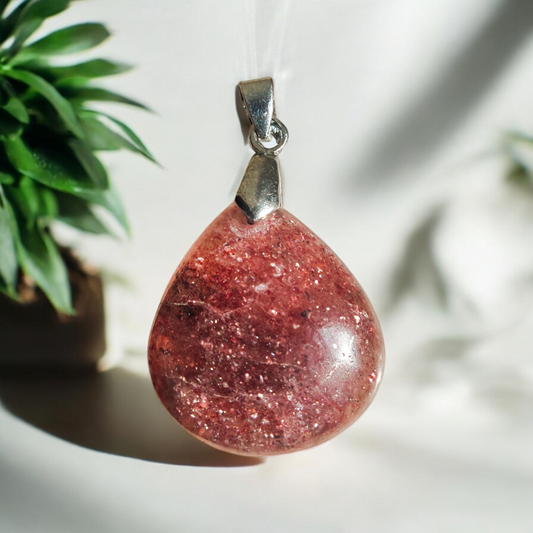 A teardrop-shaped strawberry quartz pendant with a metallic loop attached, displayed against a patterned background.