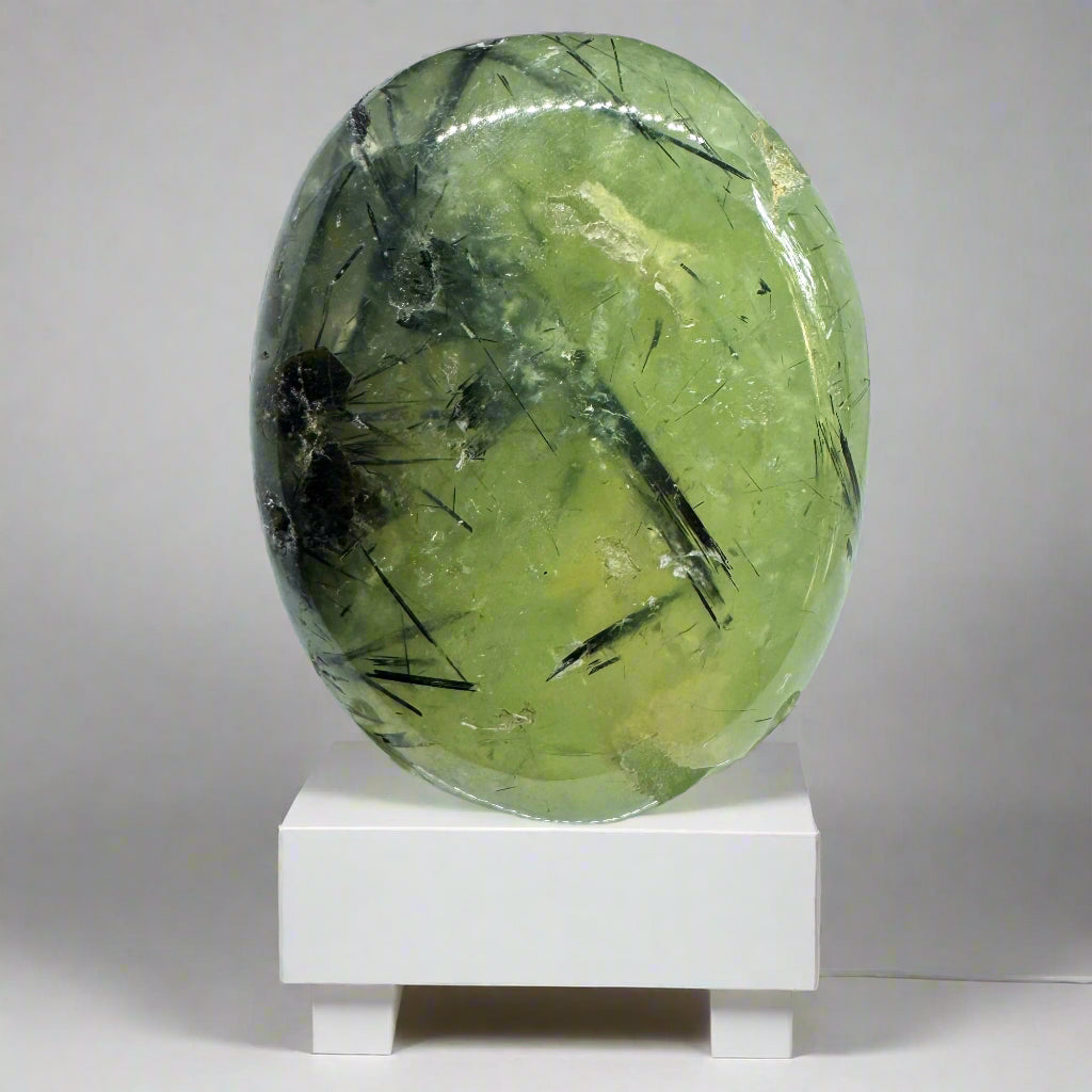 A Prehanite Palm Stone with green and black colors, displayed on a white stand.