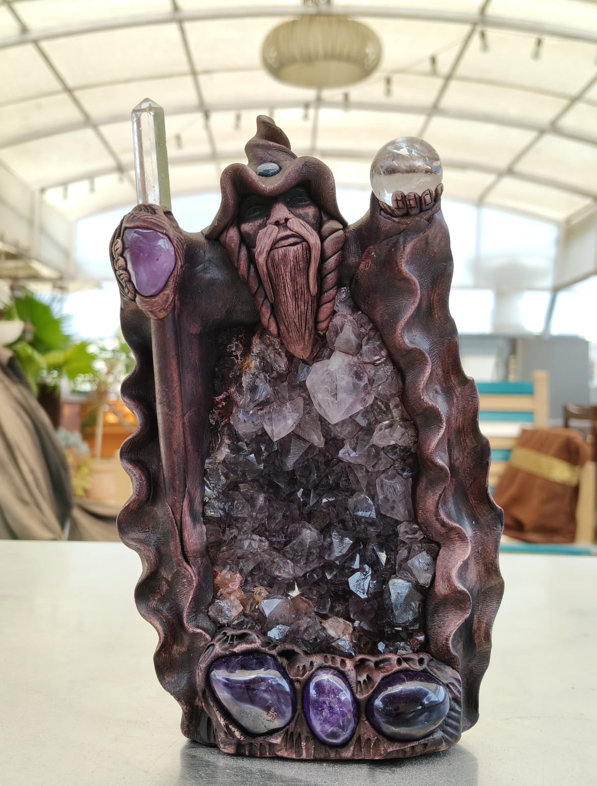 A statue of the Master Magician Merlin made with natural crystals, featuring intricate details and craftsmanship, displayed against an indoor background.